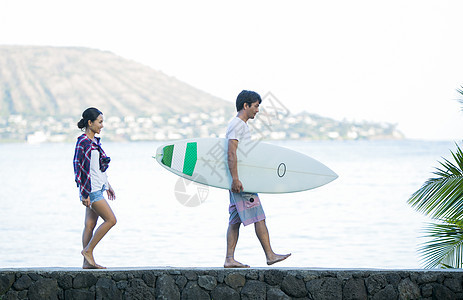冲浪夫妇拿着冲浪板沿着海滩散步图片