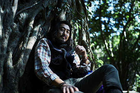 森林中徒步旅行的男人坐在树旁吹口琴休息图片