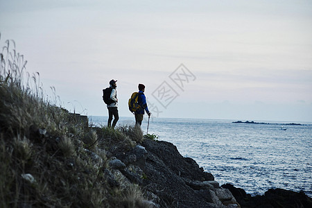 岩石上看着远方蓝色海岸线的男背包客图片