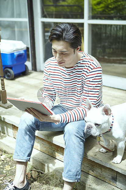 男人坐在台阶上阅读享受阳光与狗相伴图片