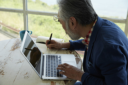 一位在窗户旁操作个人电脑的老人高清图片