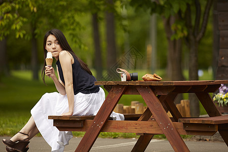 坐在公园木凳上吃冰激凌的长发美女图片