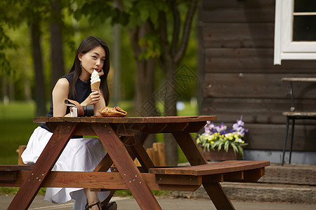 坐在公园木凳上吃冰激凌的长发美女图片