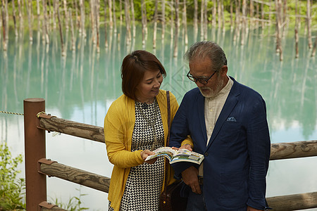 靠在湖边木围栏上看书的夫妇背景图片