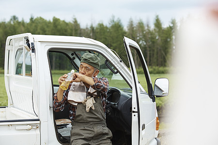 老人靠着卡车休息喝水图片