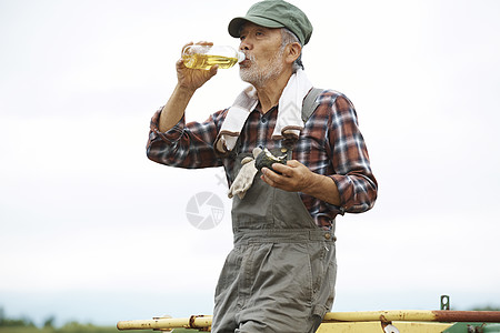 老人靠着农具休息喝水图片
