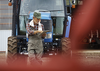 站在拖拉机前玩平板的农民图片