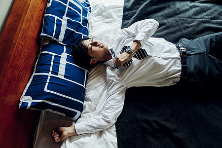 穿着衬衫领带躺在床上的年轻男性图片