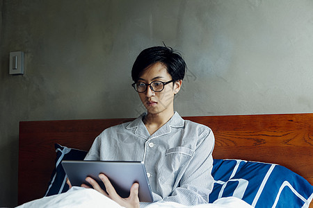 穿睡衣躺在床上是用平板电脑的年轻男性图片