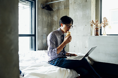 坐在床上吃面包看笔记本的男人图片