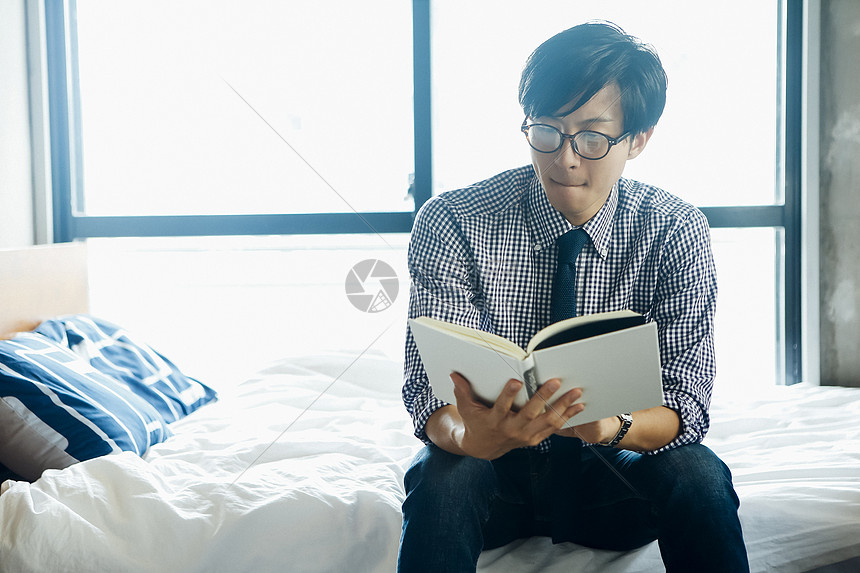 坐在床边看书的男人图片