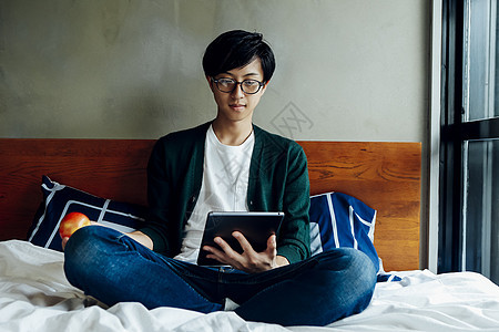 年轻男士居家在床上玩平板电脑图片