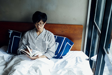 年轻男士居家在床上看书图片