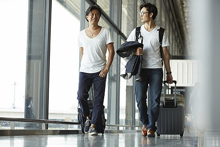 两个男人拖着行李走在机场大厅图片