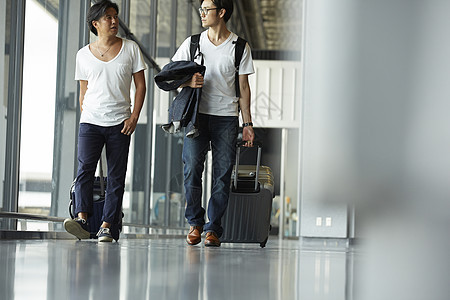 两个男人拖着行李箱走在机场大厅图片