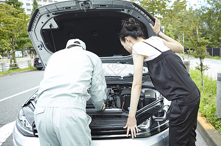 在马路上修理汽车故障的技工与女车主图片
