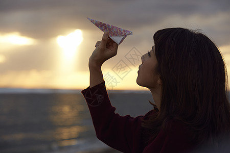 女人在夕阳下手拿纸飞机图片