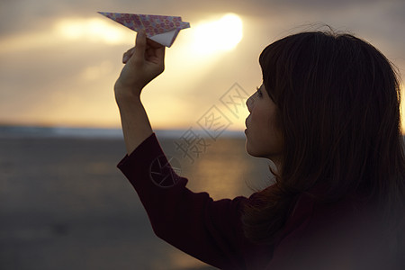 女人在夕阳下手拿纸飞机图片