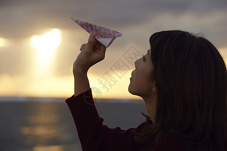 女人在夕阳下手拿纸飞机图片