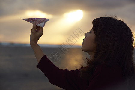 女人在夕阳下手拿纸飞机图片