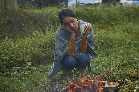 在篝火旁拿着杯子思考的女人图片