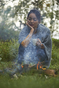 露营时蹲在篝火旁喝咖啡取暖的女性图片