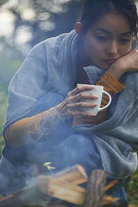 露营时蹲在篝火旁喝咖啡取暖的女性图片