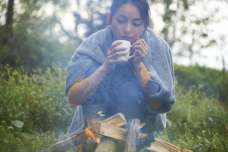 露营时蹲在篝火旁喝咖啡取暖的女性图片