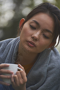 露营时蹲在篝火旁喝咖啡取暖的女性图片