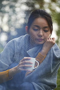 露营时蹲在篝火旁喝咖啡取暖的女性图片