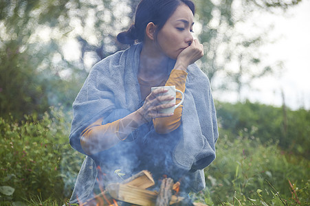 露营时蹲在篝火旁喝咖啡取暖的女性图片