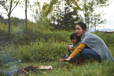 露营时蹲在篝火旁喝咖啡取暖的母子二人图片