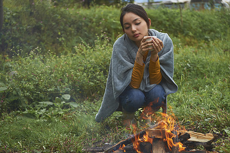 露营时蹲在篝火旁喝咖啡取暖的女性图片