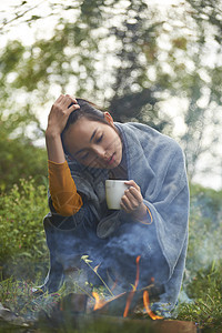 露营时蹲在篝火旁喝咖啡取暖的女性图片