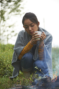 露营时蹲在篝火旁喝咖啡取暖的女性图片