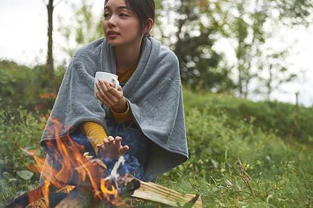 露营时蹲在篝火旁喝咖啡取暖的女性图片