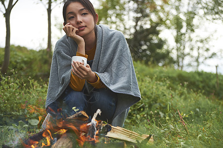 露营时蹲在篝火旁喝咖啡取暖的女性图片