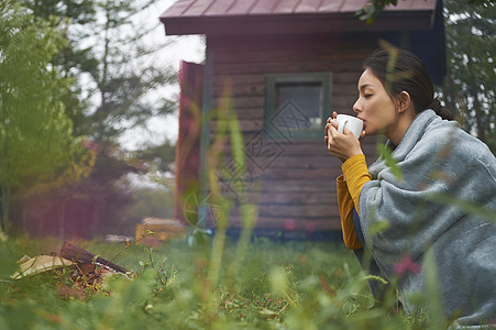 露营时蹲在篝火旁喝咖啡的女性图片