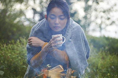 蹲在篝火旁取暖喝咖啡的女人图片