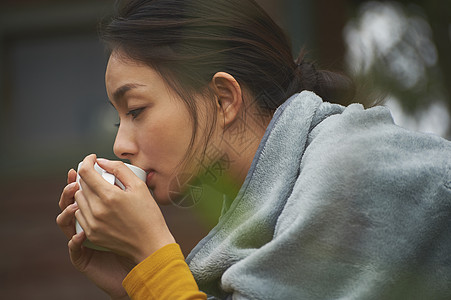 蹲在篝火旁取暖喝咖啡的女人的侧脸图片