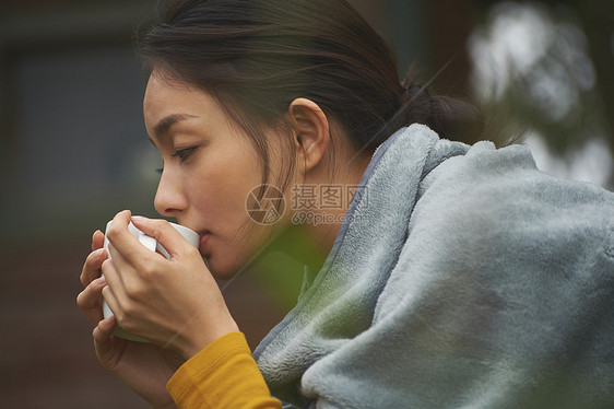 蹲在篝火旁取暖喝咖啡的女人的侧脸图片