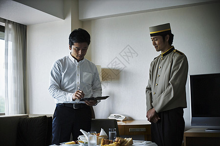 在酒店房间里给服务生付早餐费的商务人士图片