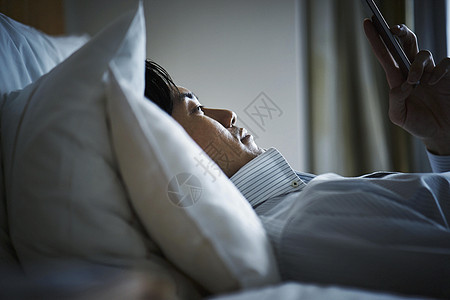 躺在旅馆床上休息看手机的商务人士图片