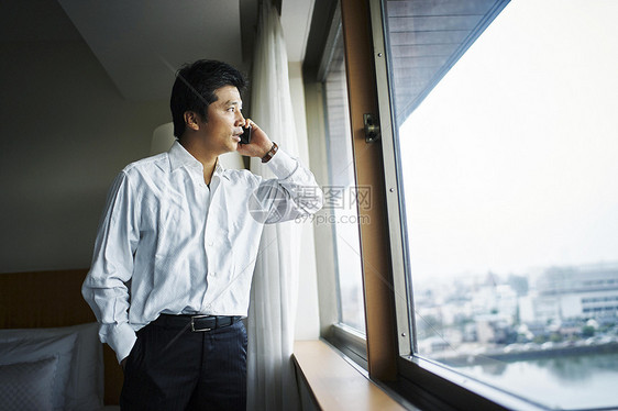 穿衬衫的都市男性站在窗前打电话图片
