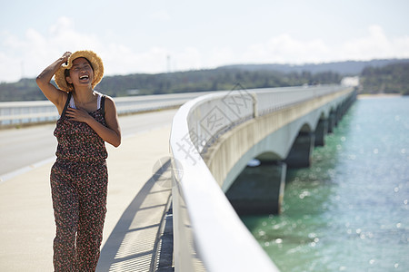 旅途中带着草帽的女性走在海面大桥上图片