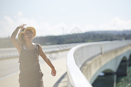 旅途中带着草帽的女性走在海面大桥上大笑图片