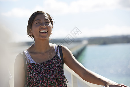 旅途中带着草帽的女性走在海面大桥上大笑图片
