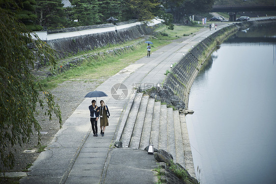 撑伞走在河堤边的年轻情侣图片