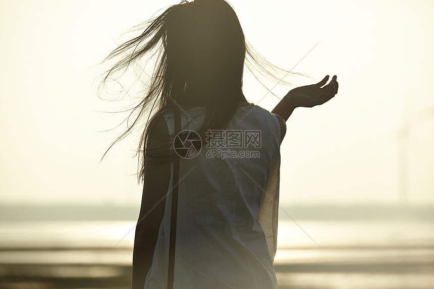 日落时女人站在湿地撩头发的剪影图片