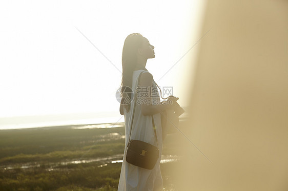 日落时分手拿相机走在海滩边上长裙美女图片